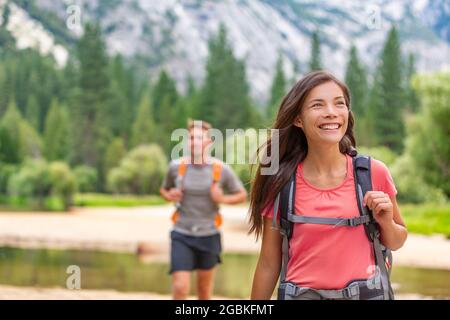 Hikers walking in nature forest of Yosemite. Happy campers hiking through trail trek in mountains. Asian girl with backpack looking up, man friend Stock Photo