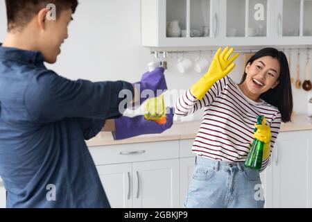 Playful asian lovers having fun while cleaning house together Stock Photo