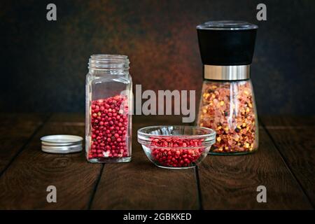 Pink pepper and a mixture of spices in glass jars on a dark background, shallow depth of field Stock Photo
