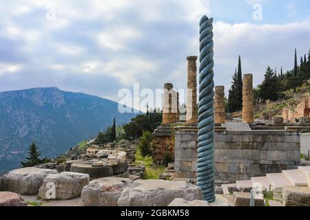 View of mountainside site of ancient Delphi Greece with twisted column in front of Temple of Apollo with a treasury down the hill and another mountain Stock Photo