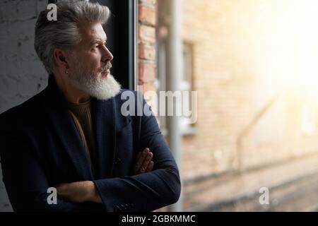 Portrait of serious middle aged man in business casual wear looking out a window while standing in loft interior Stock Photo