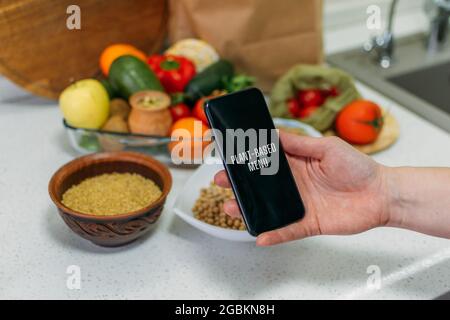 Whole-food, plant-based diet for boost health. Female hand cell phone with Plant-Based Menu recipes and healthy meal, vegetables, fruits, whole grains Stock Photo