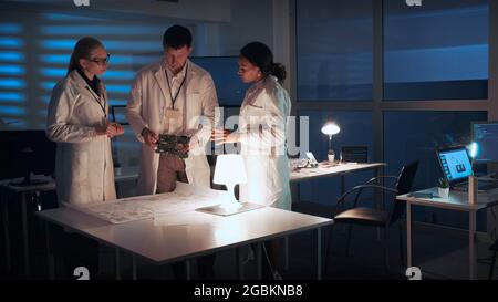 Diverse group of engineers discussing electronics development with motherboard and electronics scheme. They working in a modern lab Stock Photo