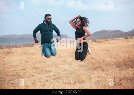 Happy young Indian couple jumping and celebrating in a field, a traveling couple Stock Photo