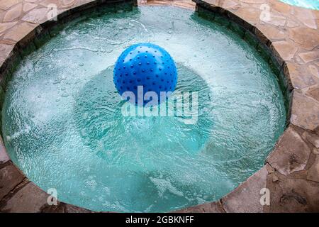 Bumpy blue beach ball floating in built-in hot tub in rock patio - top view Stock Photo