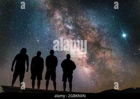 Silhouette shot of four friends watching the beautiful milky way in the night sky Stock Photo