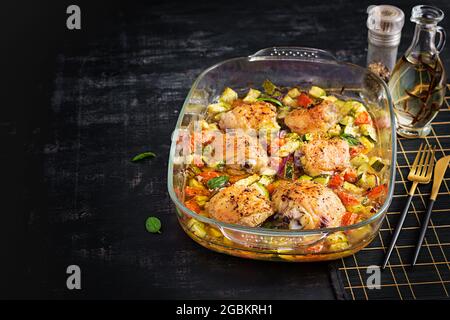 Baked chicken thighs, zucchini and vegetables in a baking dish on a dark table. Stock Photo
