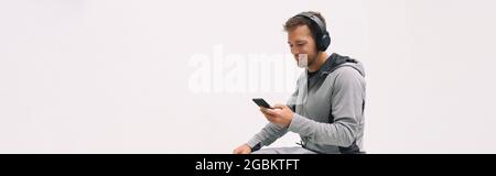 Man listening to music mobile phone app wearing headphones sitting at home white wall background panoramic. Happy guy active lifestyle sport athlete Stock Photo