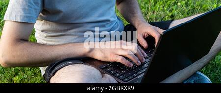 young man sitting on the grass cross-legged using a laptop Stock Photo