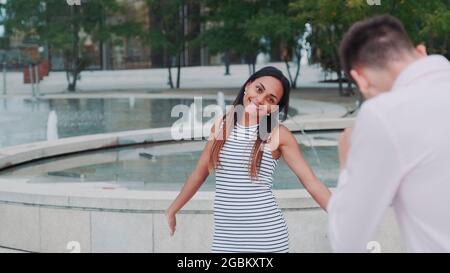 Young man taking photo of his beautiful black girlfriend in city center. Fountains are in the background. Stock Photo