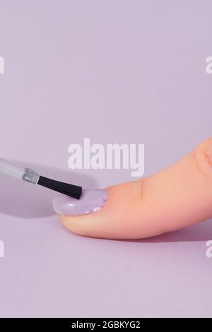 Womans hand with fashionable lavender manicure on pink background