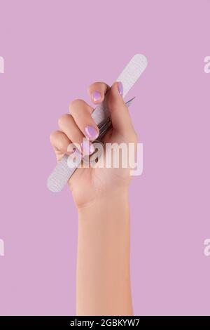 Womans hand holding manicure instrument on pastel lavender background Stock Photo
