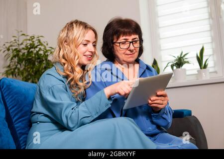 Adult daughter explaining elderly mother how to use tablet Stock Photo