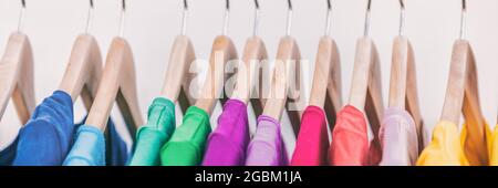 Clothes on clothing rack panoramic banner. Women's wardrobe fashion apparel rainbow organized t-shirts by colors hanging on closet hangers. Shopping Stock Photo