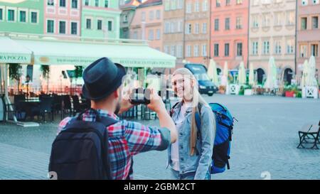 Young tourist couple making photos on the view of historical buildings. Woman posing. Man taking photos. Stock Photo