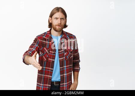Serious bearded blond man frowning, extend hand for handshake, greeting someone, nice to meet you, having business meeting, standing over white Stock Photo