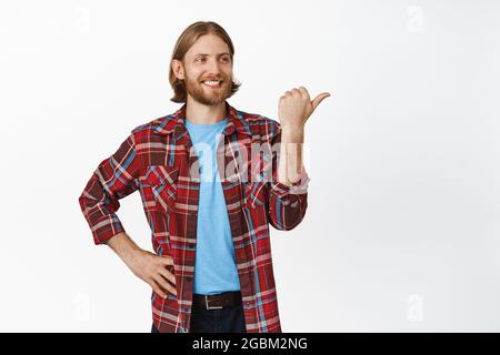 Handsome confident blond man, smiling pleased, looking and pointing right at copy space, showing advertisement with satisfied proud face expression Stock Photo