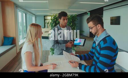 Group of diverse woman and men with tablet in modern office hall having work with documents and statistics Stock Photo
