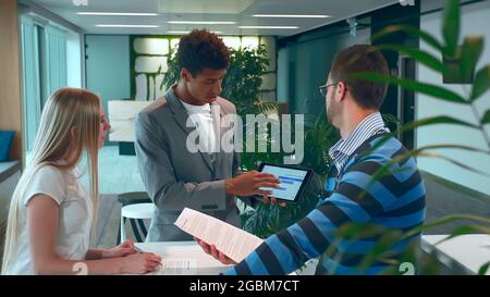 Group of diverse woman and men with tablet in modern office hall having work with documents and statistics. Stock Photo