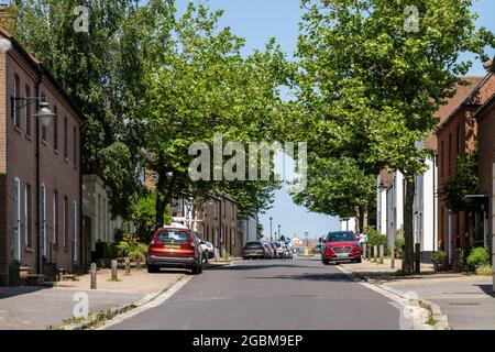 Large street trees and parked cars fill the streetscape of Middlemarsh Street, one of the first streets to be built in Poundbury new town, Dorset. Stock Photo
