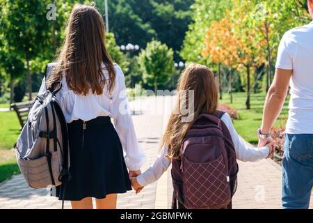 Two daughters in school uniform walking together with father to school  Stock Photo