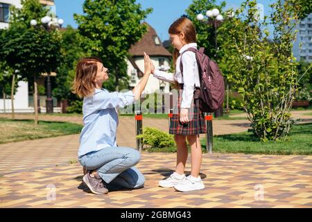 Caucasian schoolgirl with backpack and uniform says goodbye to her mother Stock Photo