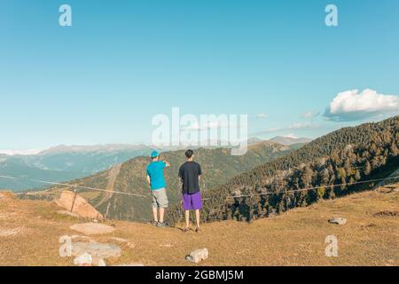 Back view of two young hikers enjoying the view of the mountains from a peak Stock Photo