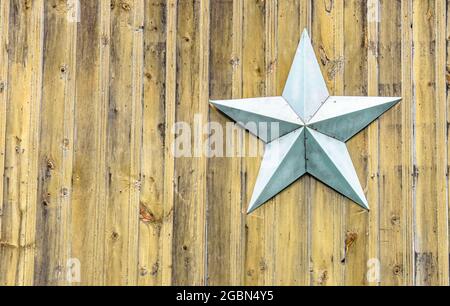 Light blue-grey metal star on a background of vertical rustic yellow pine beadboard. Copy space. Stock Photo