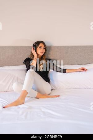 Vertical shot of a beautiful Caucasian woman on her bed while listening to music on her headphones Stock Photo