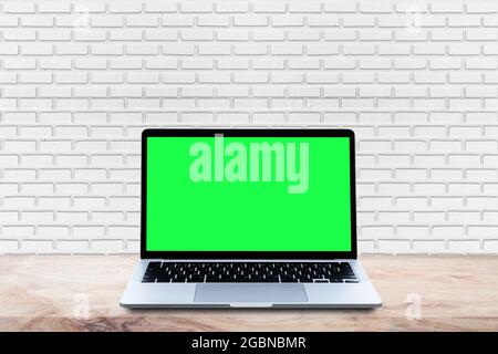 Mockup Laptop computer blank green screen on wood table with white brick wall background. Stock Photo
