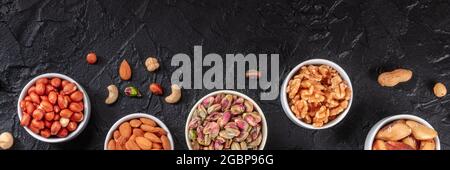 Nuts panorama with copy space, shot from the top on a black slate background. Peanuts, almonds, pistachios etc Stock Photo