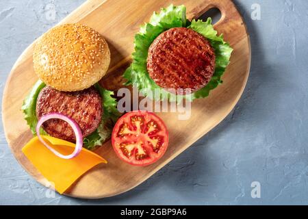 Burger, shot from the top on a blue background with a place for text. Beef hamburger patties with salad, tomato, onion and cheese, overhead shot Stock Photo