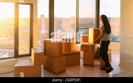 Moving into new home movers pick-up service. Woman ready to move from apartment with belongings packed in many cardboard boxes packages for shipping Stock Photo