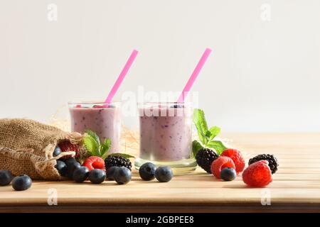 Forest berry yogurt smoothie in glass glasses on wooden table with sack full of blueberries, blackberries raspberries white isolated background Stock Photo