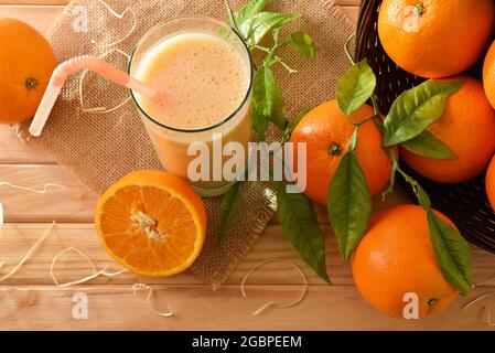 Orange milkshake and group of oranges in a basket on wooden table. Top view. Stock Photo