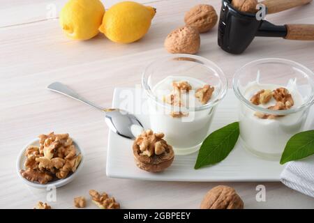 Glasses with yogurt with walnuts and bowl with walnuts and lemons on wooden kitchen bench. Elevated view. Stock Photo