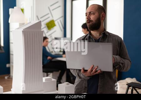 Professional man working as architect at office while using laptop computer for blueprint design. Adult constructor inspecting maquette plan bulding model for environment urban structure Stock Photo