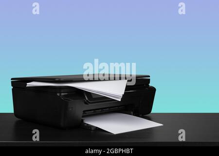 Compact laser printer on black desk against blue background Stock Photo