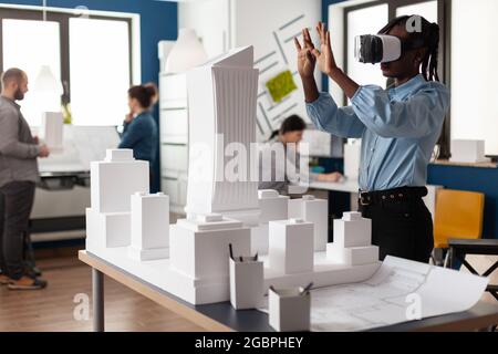 African american woman using vr glasses at work for 3d visual simulation. Standing businesswoman working on building model maquette with modern digital plan design technology Stock Photo