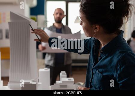 Architecture office partners looking at blueprints and plans for building model maquette. Caucasian professional workers pointing at construction design layout for urban project Stock Photo