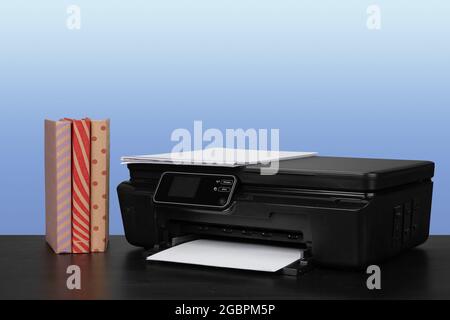 Compact laser printer on black desk against blue background Stock Photo