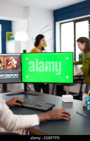 Black woman video editor with headphones using with green screen, chroma key mockup computer with isolated display sitting in start-up production studio. African videographer processing film montage Stock Photo