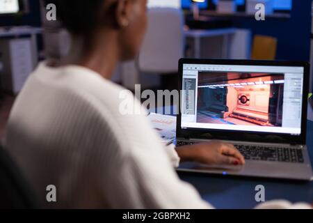 African american game developer testing new game working late at night in creativity agency company. Tired creator designer developing online video games on pc using modern production technology Stock Photo