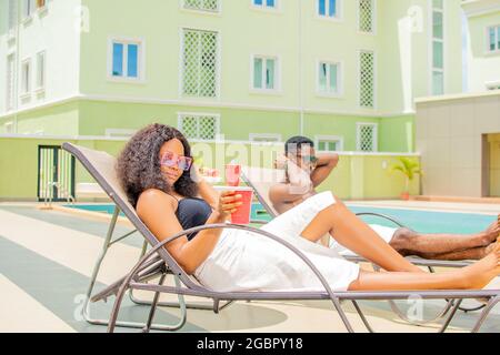 attractive young black woman relaxing by the pool alongside another guy. Stock Photo
