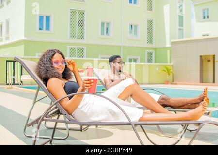 attractive young black woman relaxing by the pool alongside another young man, holiday vibes Stock Photo