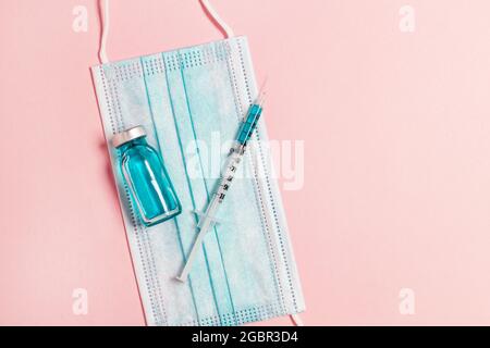 Vial vaccine, glass ampoules and syringe with a medicine, medical protective mask on pink background. Gdobal vaccination, adults and children Stock Photo