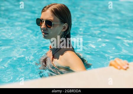Beautiful young tanned woman in sunglasses, in the outdoor pool, woman in a swimsuit sunbathing in the pool, Happy woman relaxing in the pool, The con Stock Photo