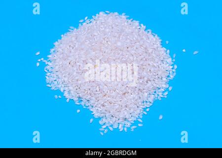 a handful of uncooked white rice on blue background. concept food, kitchen and healthy life Stock Photo