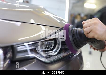 Master repairman polishing headlights of car in workshop using machine closeup Stock Photo