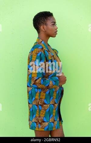 Young black female in traditional African piece of fabric looking away against pistachio background Stock Photo